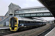 A two coach train beneath a lattice bridge