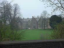 stone building with slate roof, with windows on central two bays, partly obscured by trees