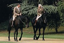 Elizabeth and Ronald Reagan on black horses. He bare-headed; she in a headscarf; both in tweeds, jodhpurs and riding boots.