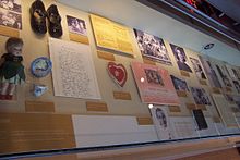 Museum display case containing photographs, papers, shoes, doll, and other early childhood artifacts