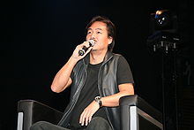 A man sitting in a chair and speaking in a microphone