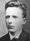 Headshot photo of a young man, similar in appearance to his brother, but neat, well-groomed and calm.